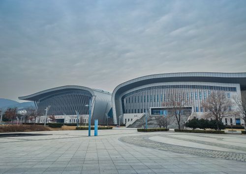 Free A modern building with striking curved facades under an overcast sky, featuring trees and pavement. Stock Photo