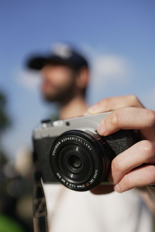 Free A close-up view of a person holding a camera, with a blurred background and blue sky. Stock Photo
