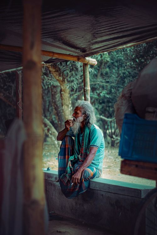 Free Elderly man with a beard in a serene outdoor setting, sitting under a rustic shelter. Stock Photo