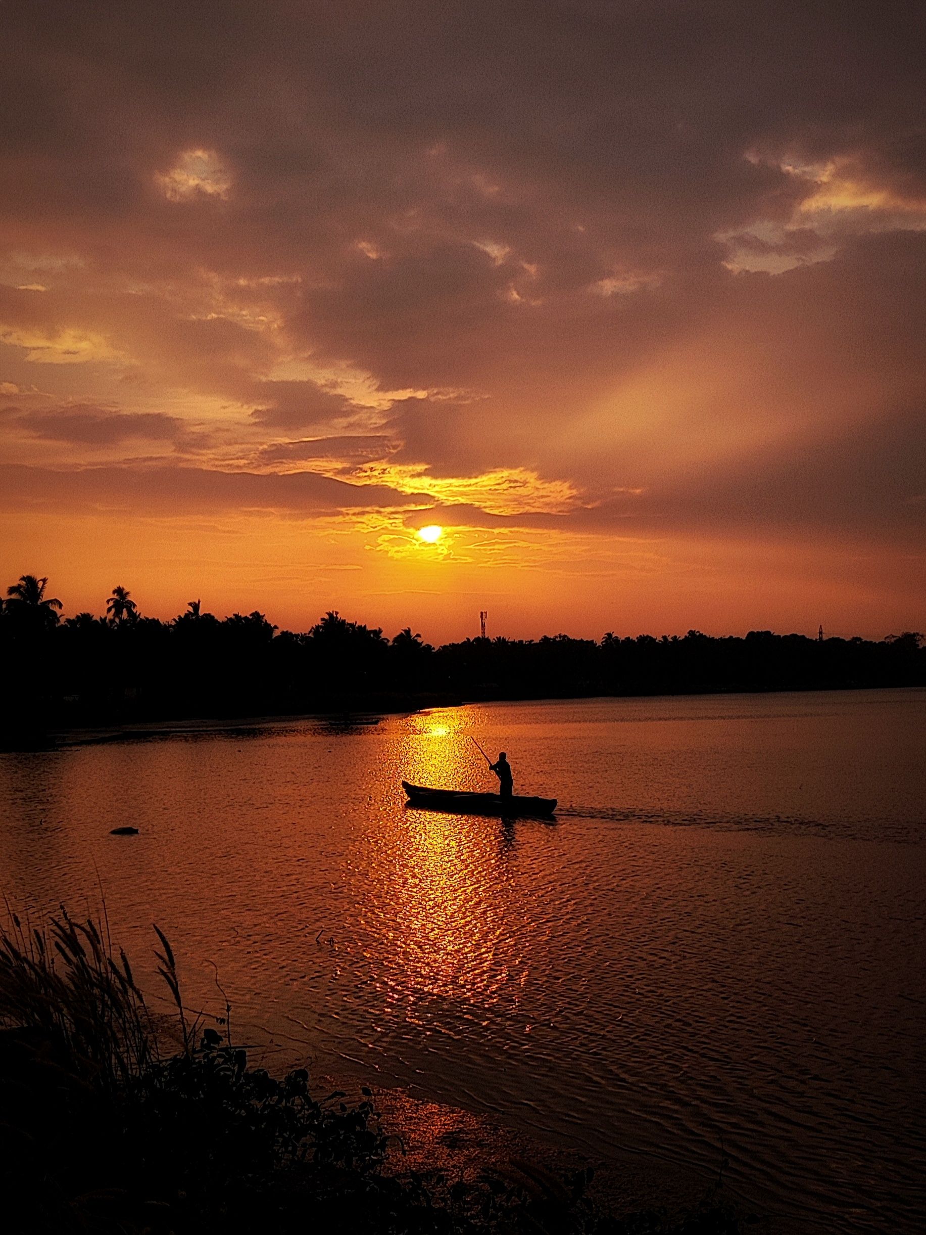 A lone fisherman in a boat under a fiery sunset sky