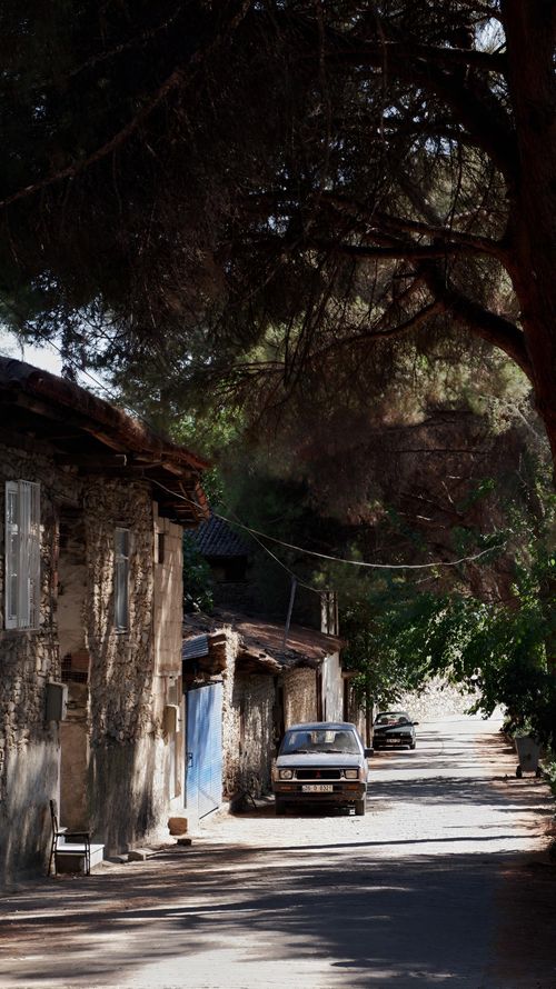 Free Charming rural street scene featuring a vintage car parked beside rustic houses and lush trees. Stock Photo