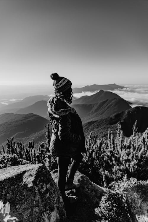 Woman in a Hat and Jacket Standing on a Mountain Peak 