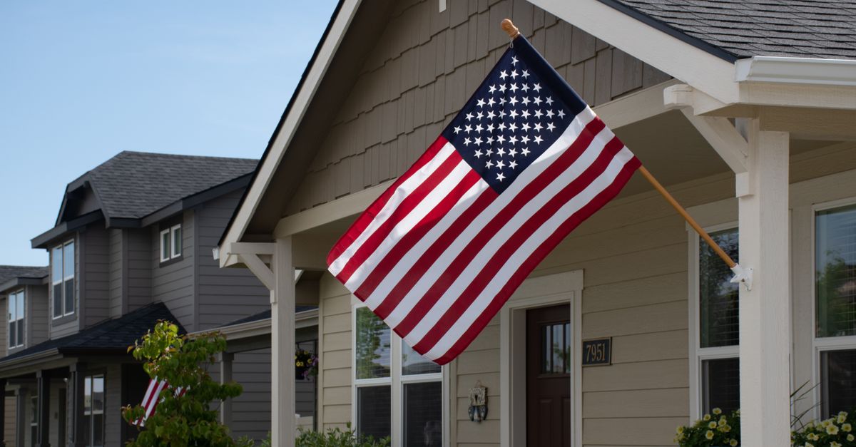 A vibrant American flag displayed outside a stylish suburban house in daylight.