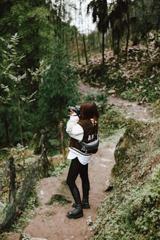 Woman taking photos on a scenic forest path, capturing nature's beauty.