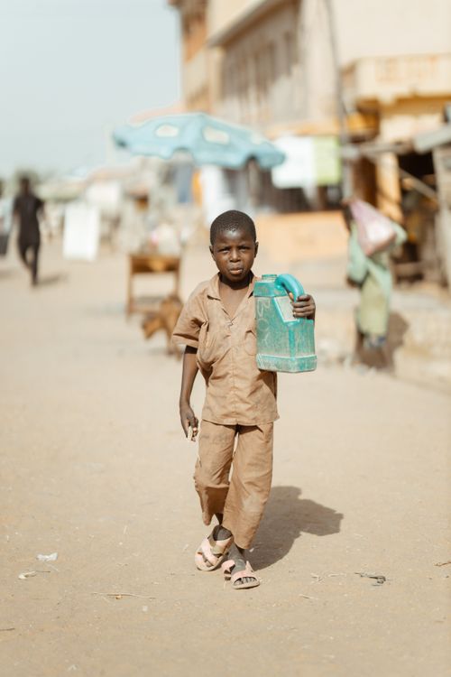 Free Young boy in casual attire carrying a blue container while walking on a bright city street. Stock Photo