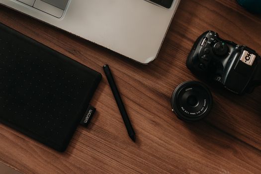 A top view of a digital workspace featuring a camera, tablet, pen, and laptop on a wooden desk.