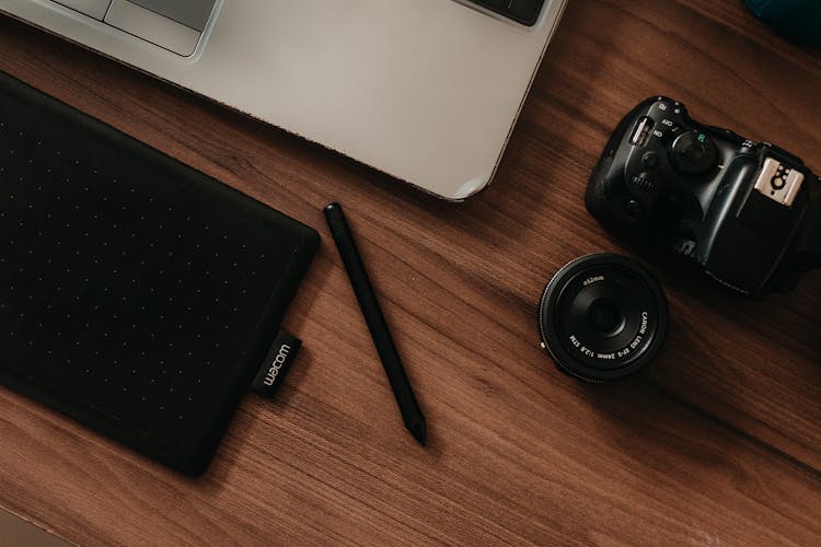 Top View Of A Laptop, Camera And A Graphic Tablet With A Pen Lying On A Desk 