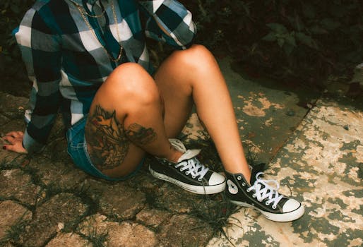 A woman in casual attire displays a vibrant leg tattoo while sitting outdoors.