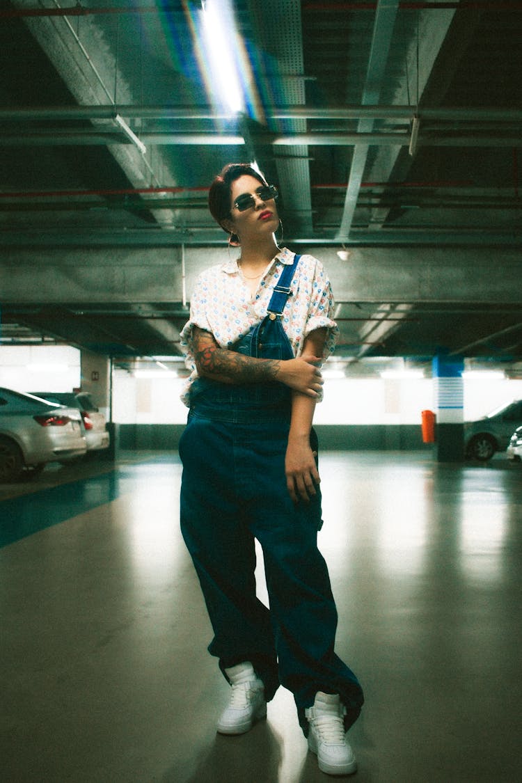 Young Woman With Tattoos Wearing Denim Overalls On A Parking Lot 