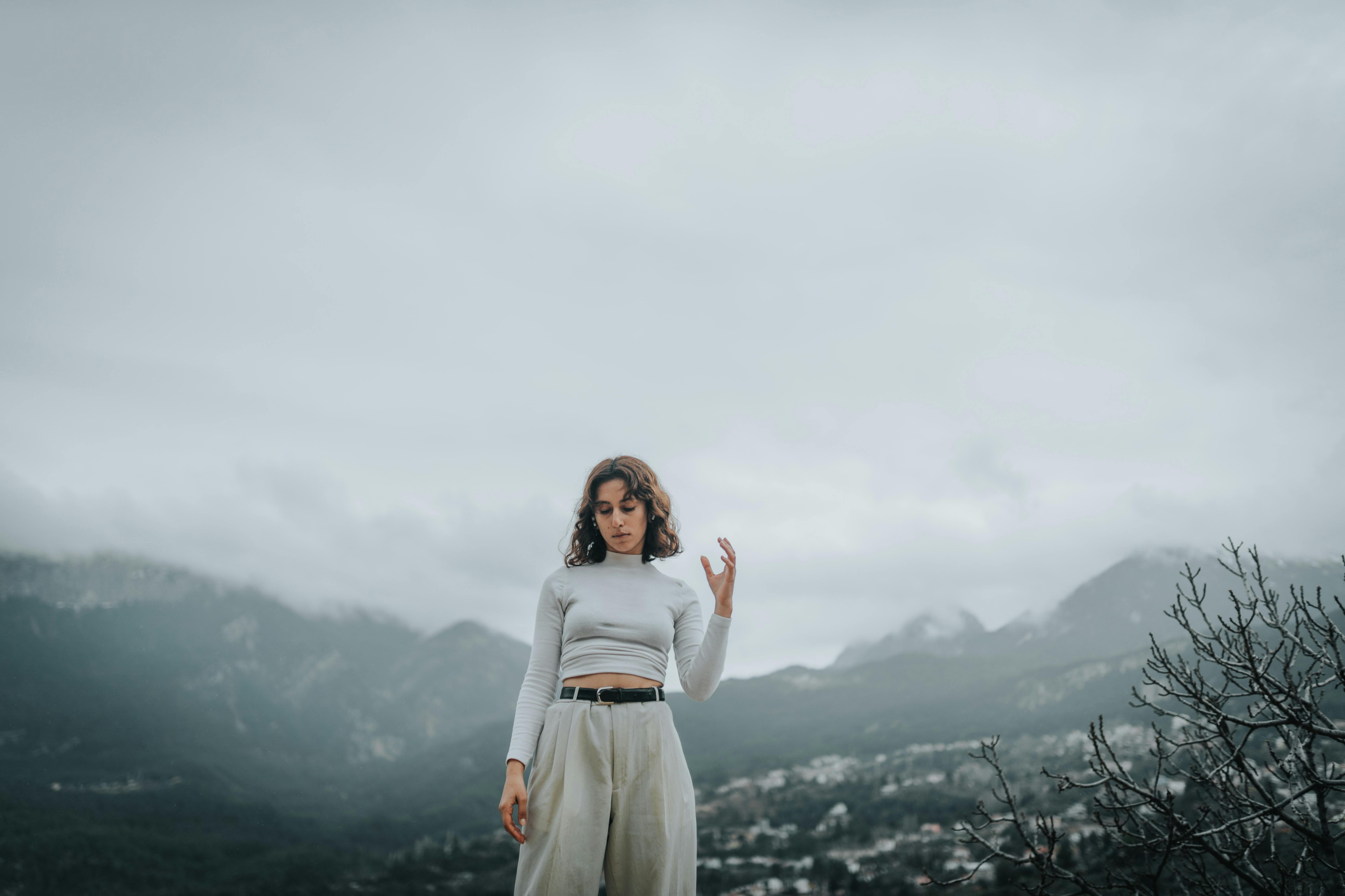 Woman posing in a stylish outfit with misty mountains in the background, exuding elegance and tranquility.