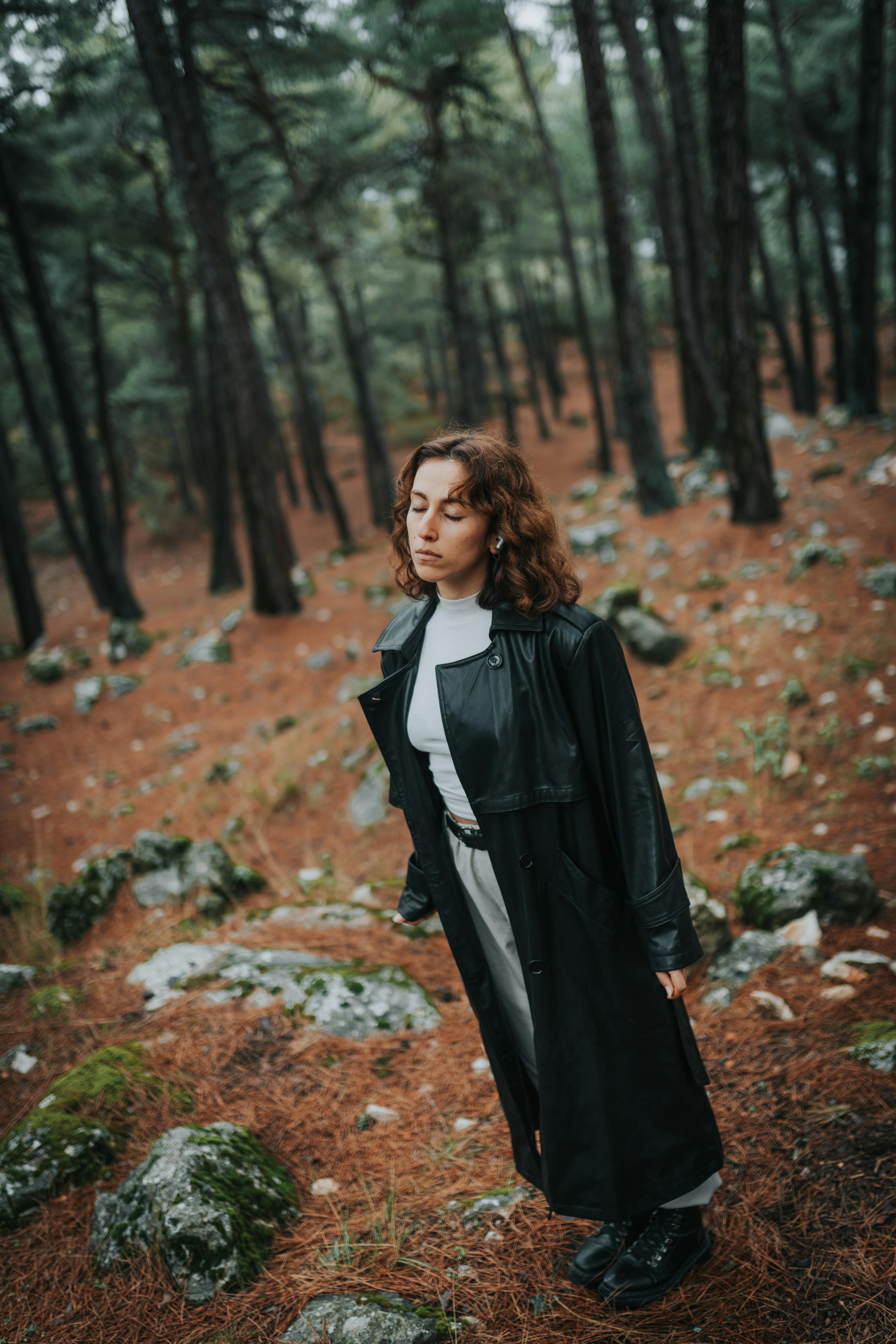 Brunette woman with eyes closed posing in a peaceful woodland setting.