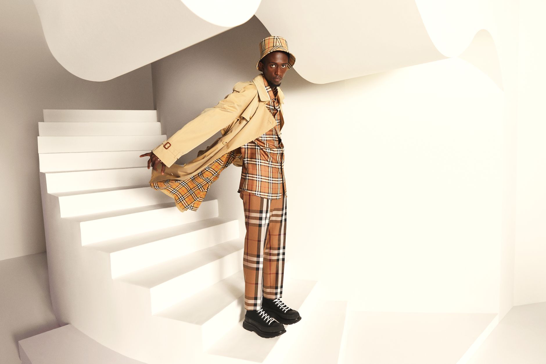Stylish man in tan plaid outfit posing on white staircase indoors.