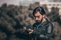 一位时尚的男性摄影师戴着太阳镜，在户外检查数码单反相机