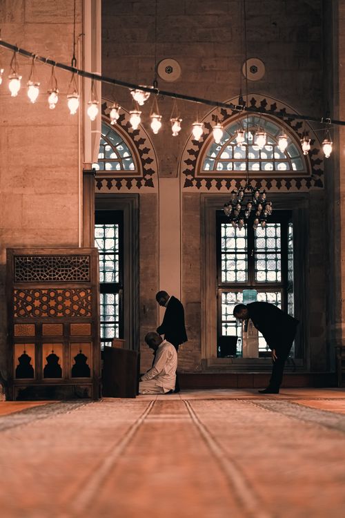 Free Peaceful mosque interior with worshipers in prayer under elegant arches and chandeliers. Stock Photo