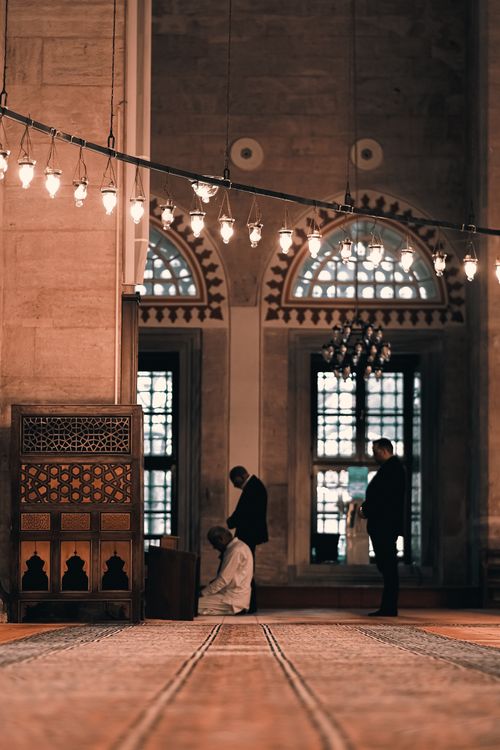 Free Atmospheric view of a mosque's interior with people praying, featuring intricate architectural details. Stock Photo