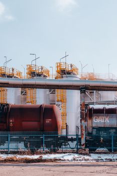 Freight trains in front of storage tanks at an industrial site in winter.