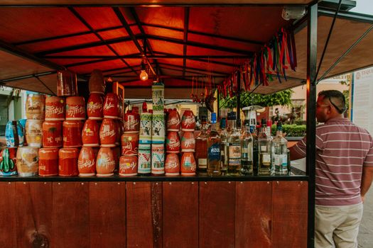 Outdoor street bar with vibrant jars and bottles, a man standing, and festive ribbons.