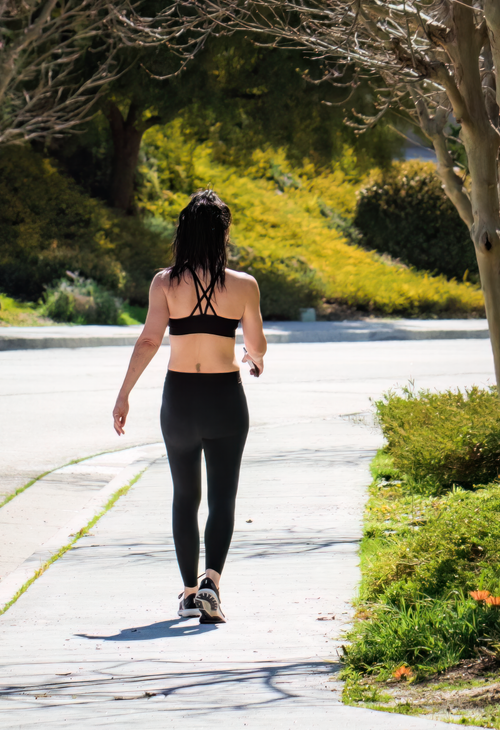 Free A woman exercises while strolling on a city sidewalk in activewear on a bright, sunny day. Stock Photo