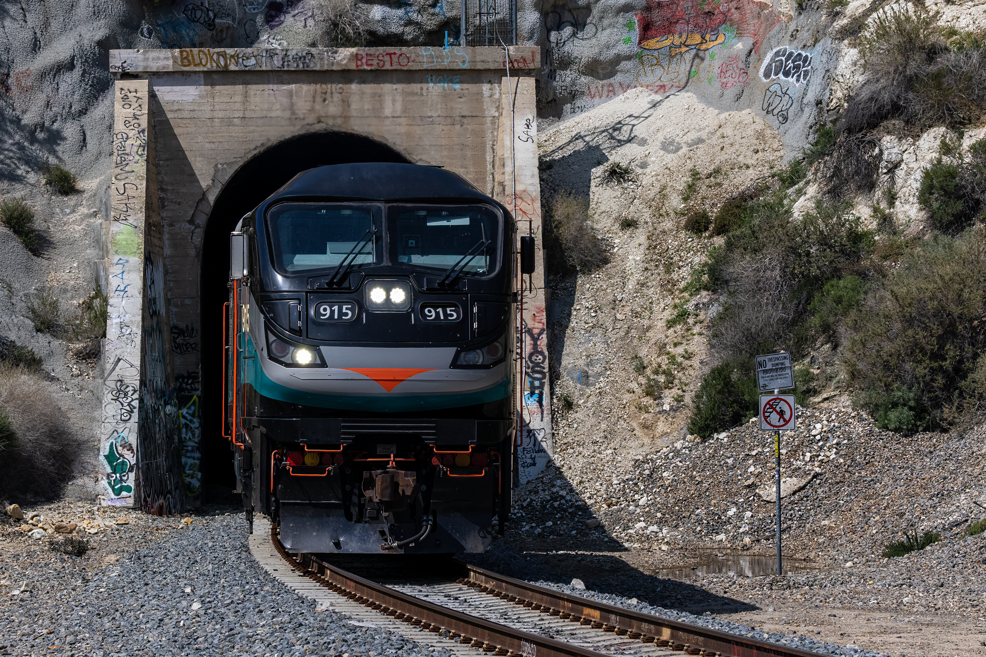 Train exiting a graffiti-covered tunnel in a rocky outdoor setting, showcasing transportation.