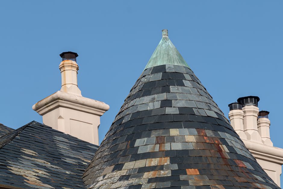 Close-up of a residential building's chimney and copper-topped tiled roof against a clear blue sky.