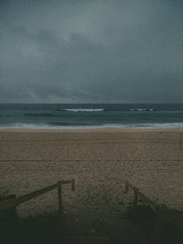 A serene beach under an overcast sky at twilight, capturing a calm and moody seascape.