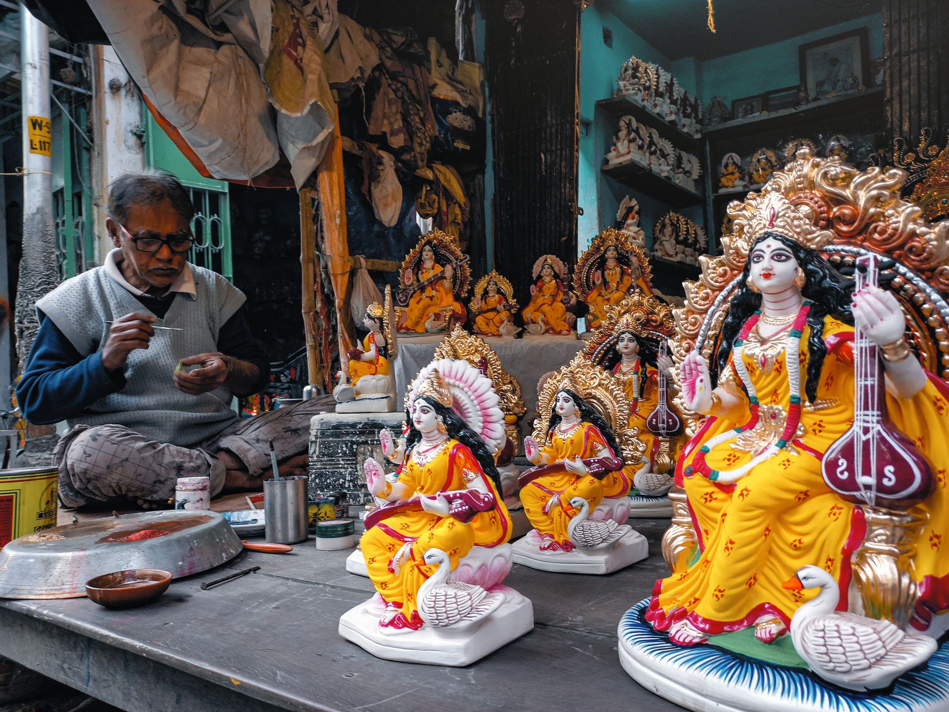 Artisan meticulously paints Hindu goddess figurines at a vibrant market stall in Kolkata, India.
