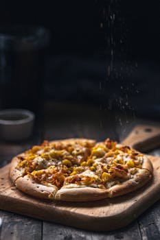 Delicious homemade pizza topped with corn and cheese, served on a wooden board with seasoning sprinkle.