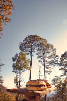 Delicious burgers served on a cutting board against a forest backdrop under a clear blue sky.