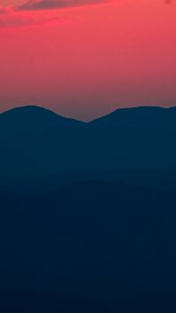 Serene silhouette of mountains against a vibrant pink sky during sunset, creating a captivating scenic view.