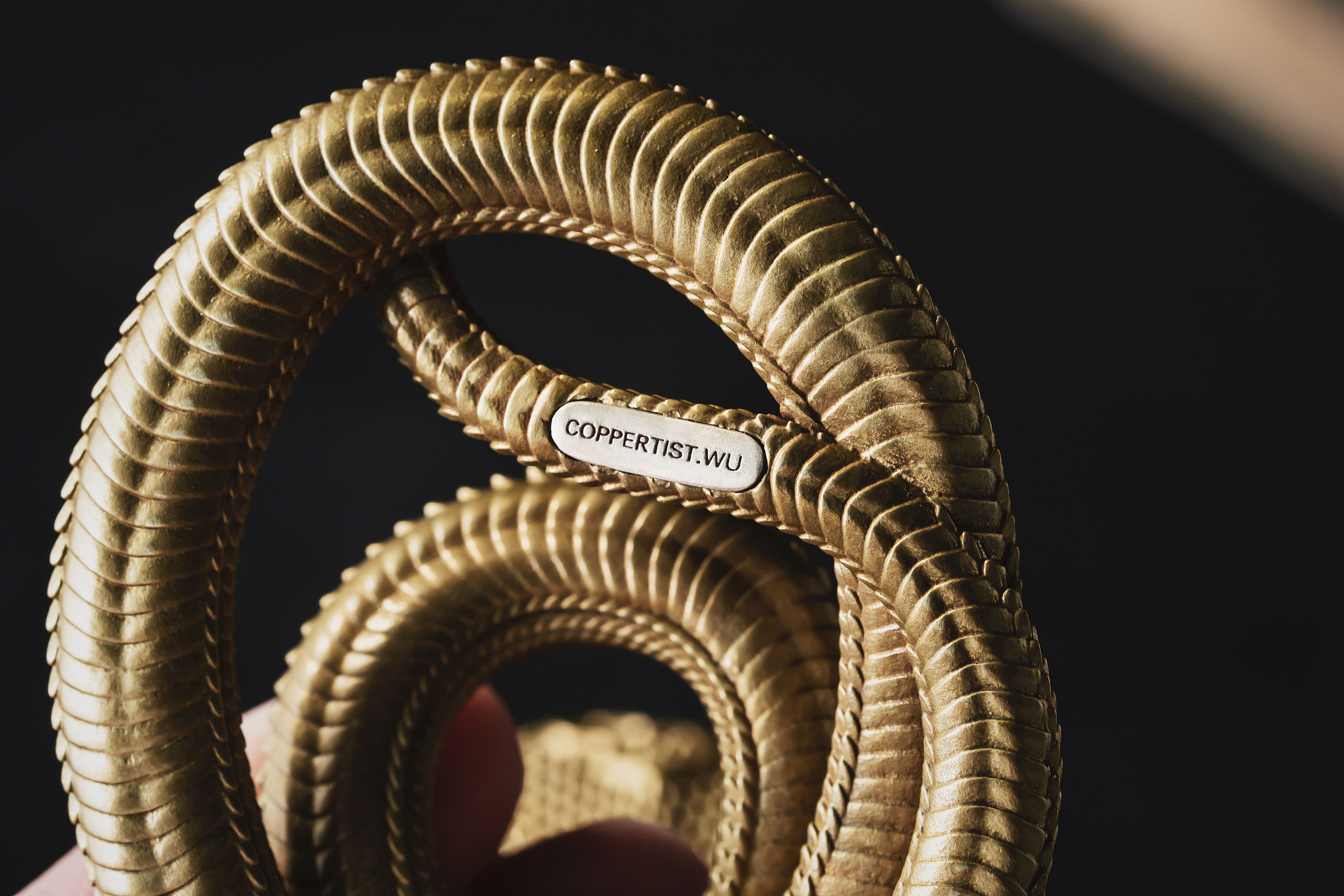 Detailed close-up of a handcrafted golden cobra phone stand on a black background.