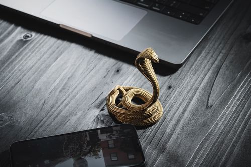 Free Close-up of a handmade golden cobra phone stand elegantly placed on a wooden desk beside a laptop. Stock Photo