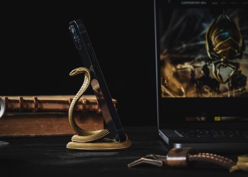 Free Golden cobra-shaped metal phone stand holding a smartphone on an elegant desk setup. Stock Photo