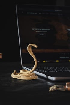 Close-up of a handcrafted golden cobra-shaped phone stand next to a laptop on a desk.