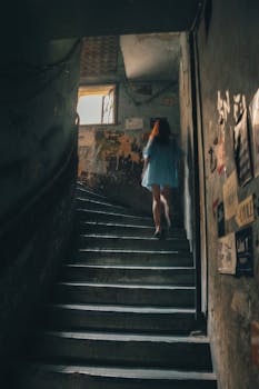 一名身穿蓝色连衣裙的女子登上楼梯，灯光昏暗，营造出一种神秘的气氛