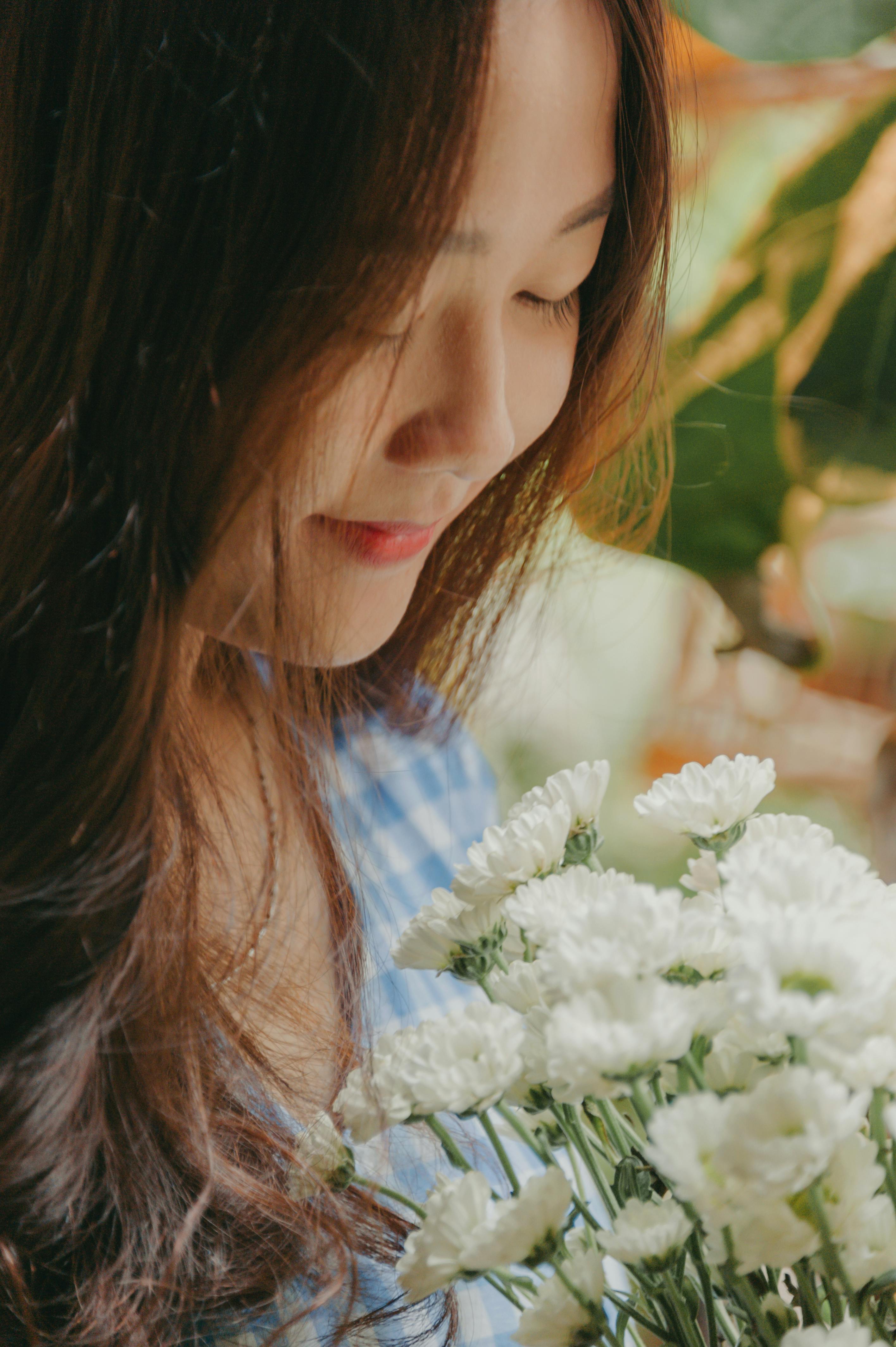 宁静的环境中，一名女子手持白花，温柔地微笑着