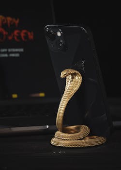 A close-up of a gold-metal cobra phone stand holding a smartphone against a dark background.