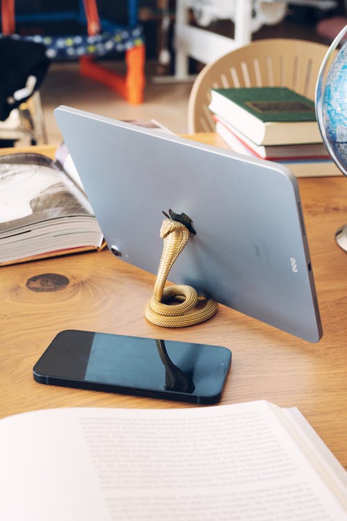 Decorative Snake-shaped Phone Stand with a Tablet on the Desk Next to a Smartphone and Books