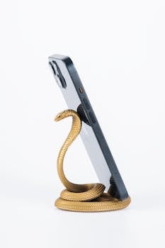 Stylish snake-shaped brass phone stand holding a smartphone on a white background, perfect for decoration and functionality.
