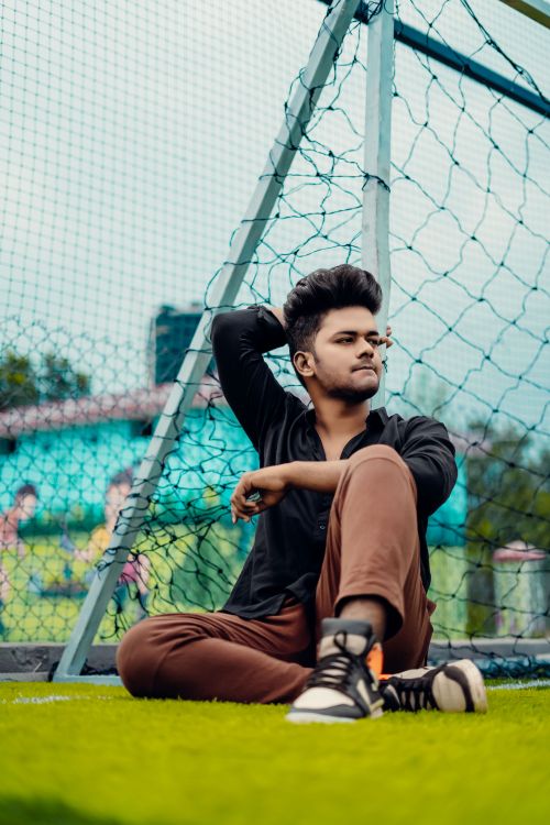 Free Young man casually sitting by a soccer goal on a vibrant football pitch. Stock Photo
