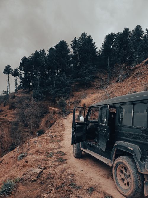 Free A rugged 4x4 vehicle on a dirt path through scenic forested mountains, perfect for adventure travel. Stock Photo