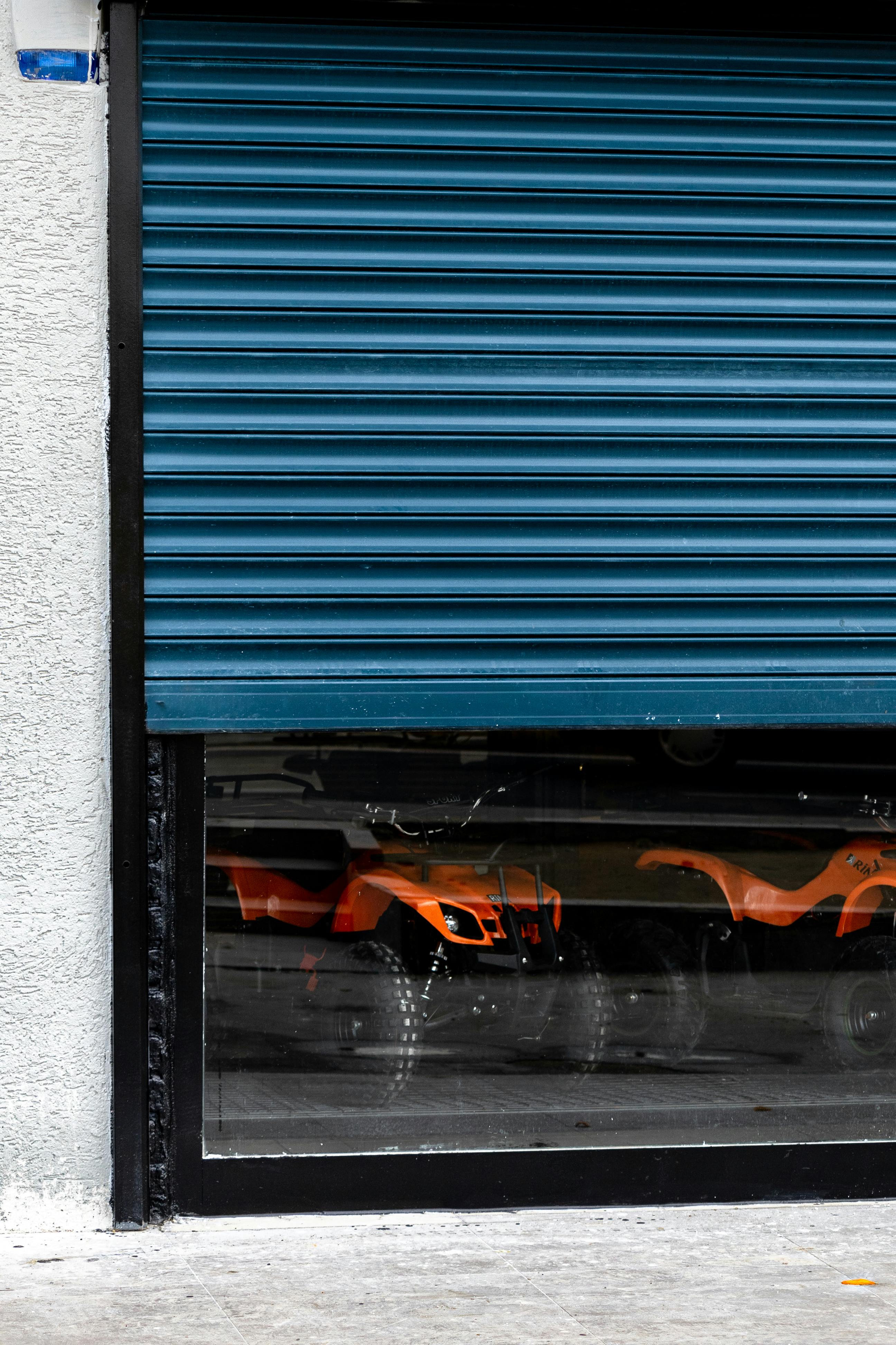 Partial view of orange ATVs behind a blue shutter, reflecting urban life.