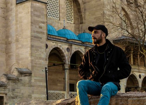 Free A man in casual attire sits near a historic mosque at sunset. Stock Photo