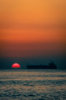 A stunning scene with a cargo ship silhouette against an orange sunset over the calm sea.