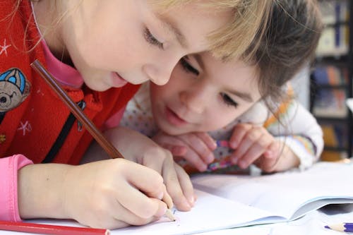 Girls on desk looking at notebook while one of them is writing on it.