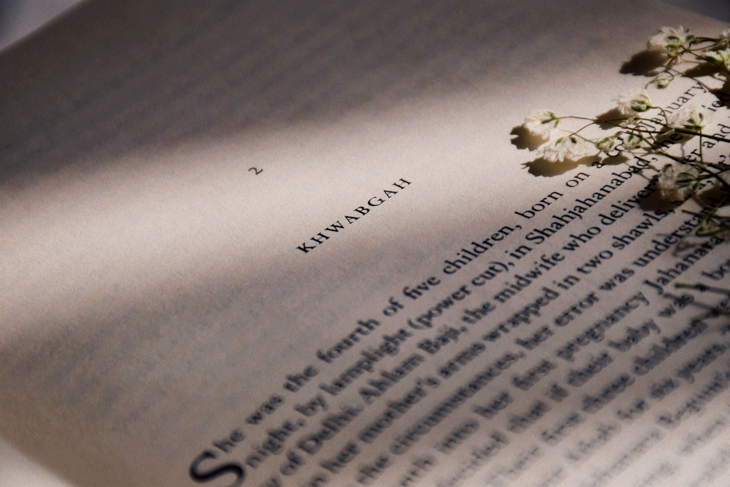 Close-up of an open book with khwabgah text, embellished with delicate pressed flowers and soft shadows.
