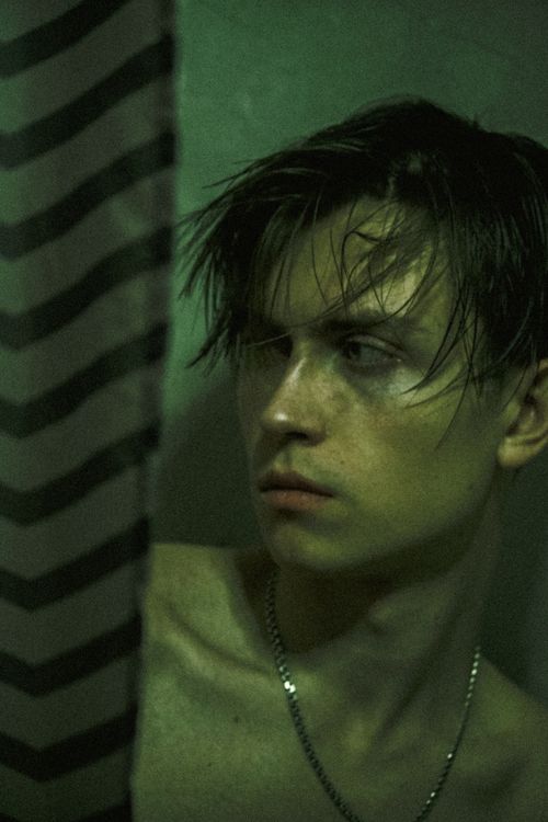 Free Dramatic portrait of a young man with wet hair beside a curtain, showcasing moody lighting. Stock Photo