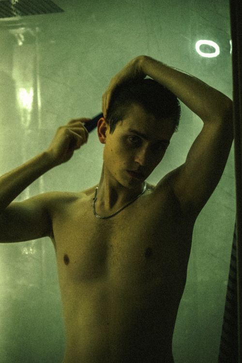 Free Shirtless young man combing his hair in a dimly lit bathroom setting. Stock Photo