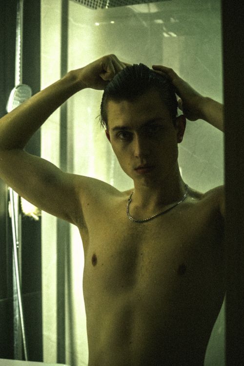 Free Portrait of a man styling his short hair in a dimly lit shower, creating a moody atmosphere. Stock Photo