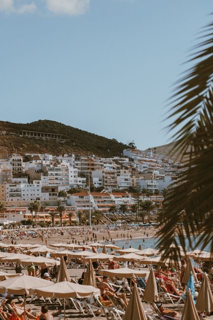 Scenic view of a vibrant beach resort with umbrellas, people, and a hillside village under a clear sky.