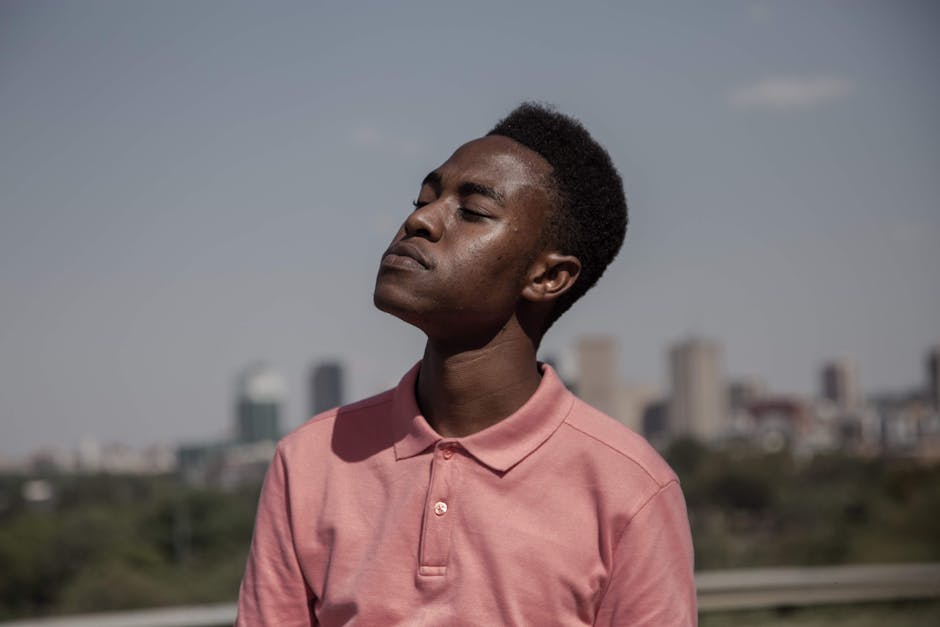 Black male in a pink shirt enjoying the daylight with city skyline in the background.